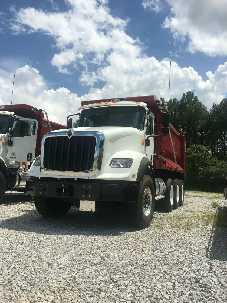 Two H&M dump trucks parked in a gravel lot