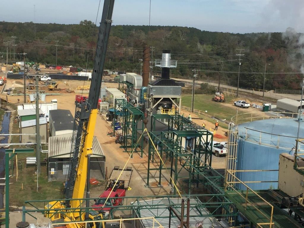 Crane erecting structural steel among process piping in an operating plant