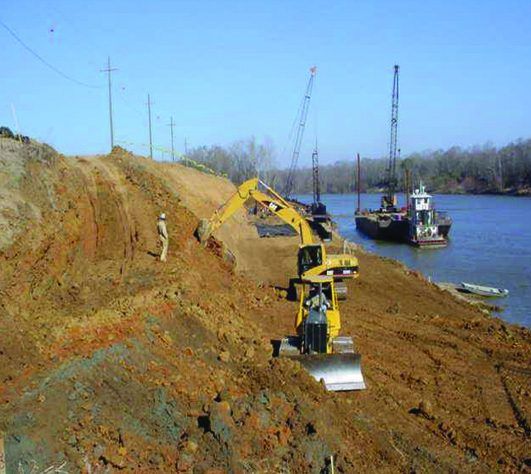 Excavator placing material along a riverbank stabilization project